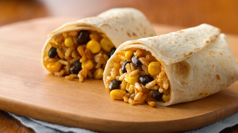 Deux burritos sur une planche de bois remplie de riz, de maïs et de haricots noirs